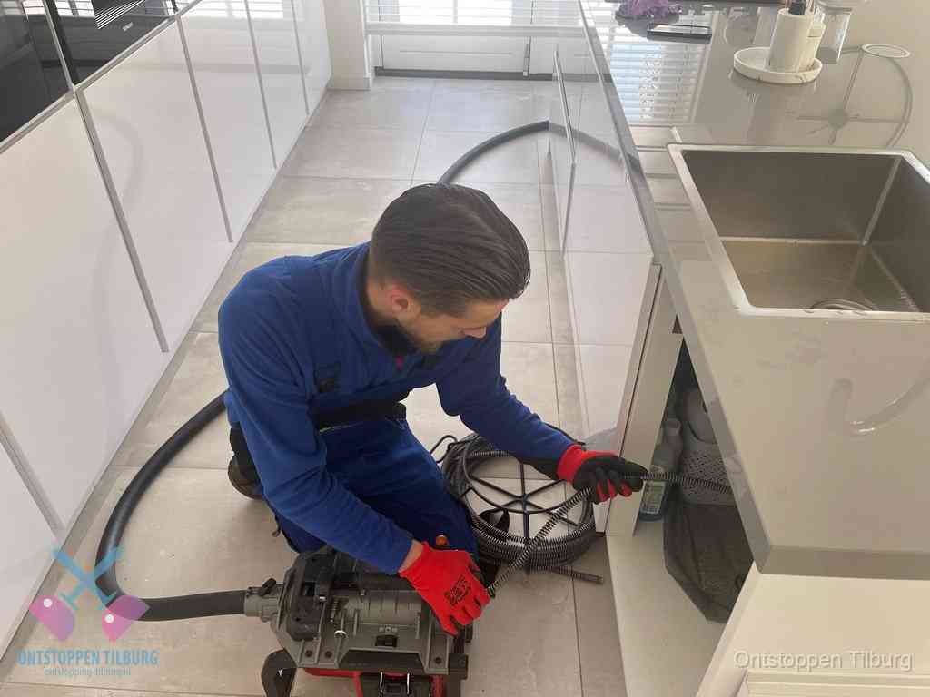 Een monteur ontstopt de keukenafvoer onder de spoelbak met een elektrische veermachine in Tilburg