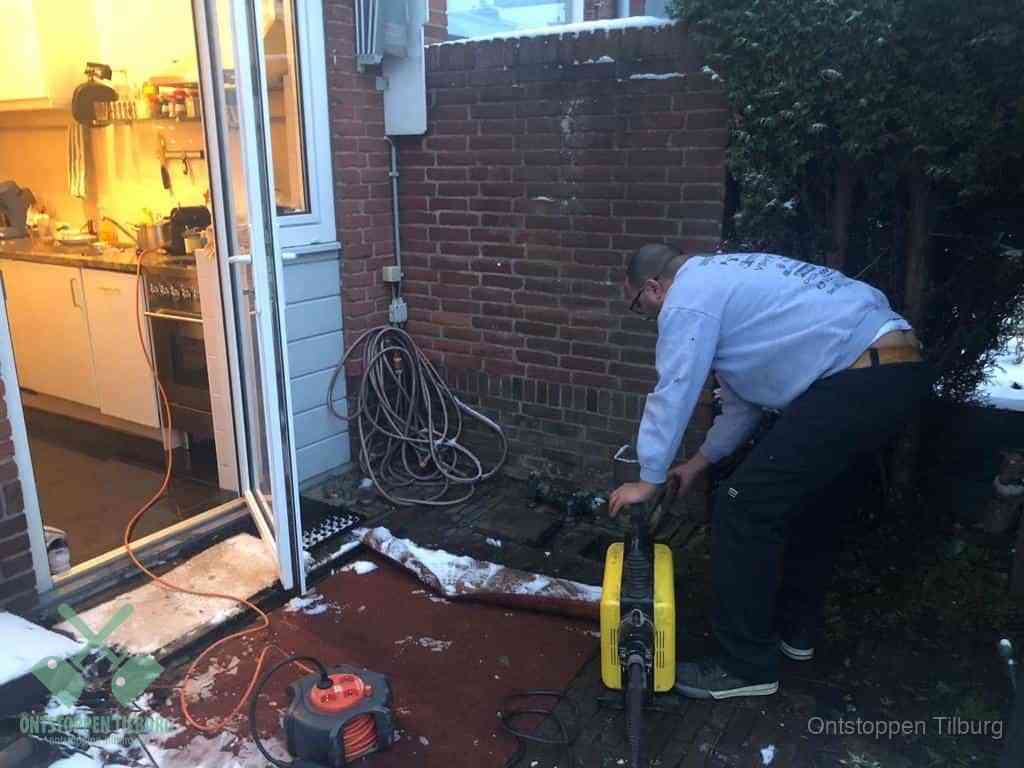Een monteur werkt buiten bij een open riool-/grondput met een elektrische ontstoppingsmachine om een verborgen afvoerprobleem op te sporen in Tilburg