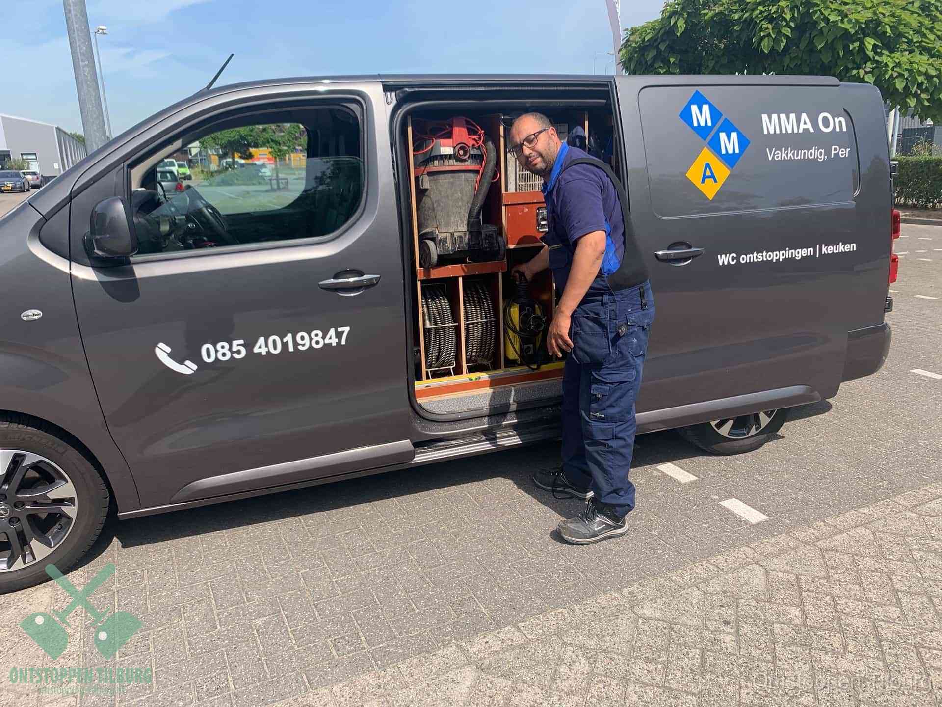 Een monteur bij de open schuifdeur van zijn bedrijfsbus op een parkeerplaats, klaar om de oorzaak van terugkerende afvoerverstoppingen aan te pakken in Tilburg