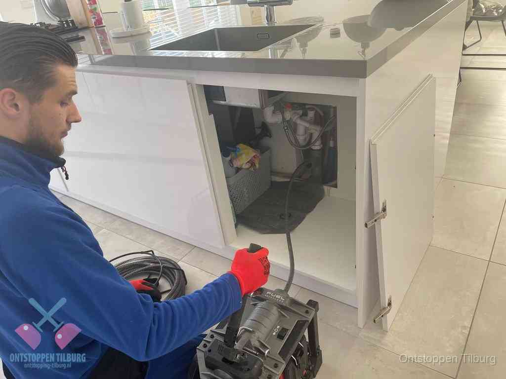 Monteur ontstopt met een veermachine een verstopte afvoer onder de gootsteen in Tilburg
