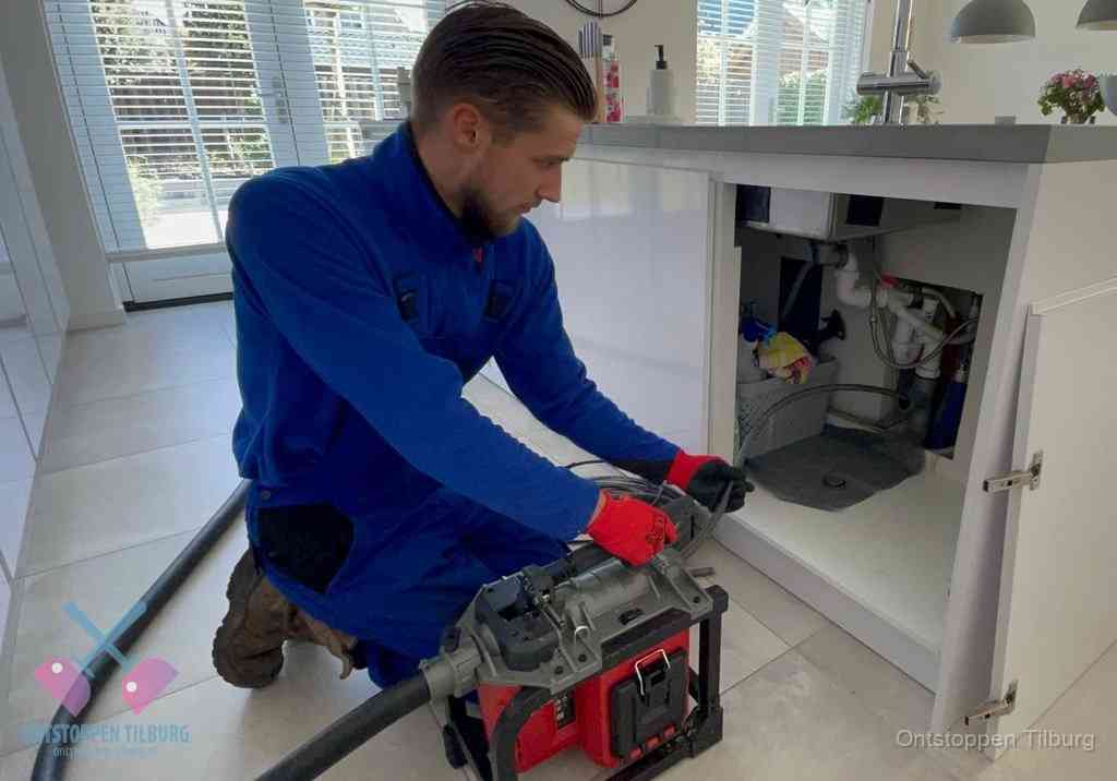 Een monteur voert een professionele elektrische ontstoppingsmachine in de afvoer onder de spoelbak tijdens het gootsteen ontstoppen in Tilburg